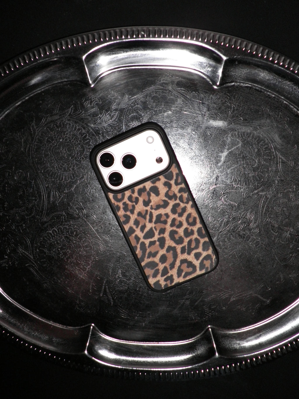 A smartphone case with a brown and black leopard print pattern, shown on a silver metal tray against a black background.