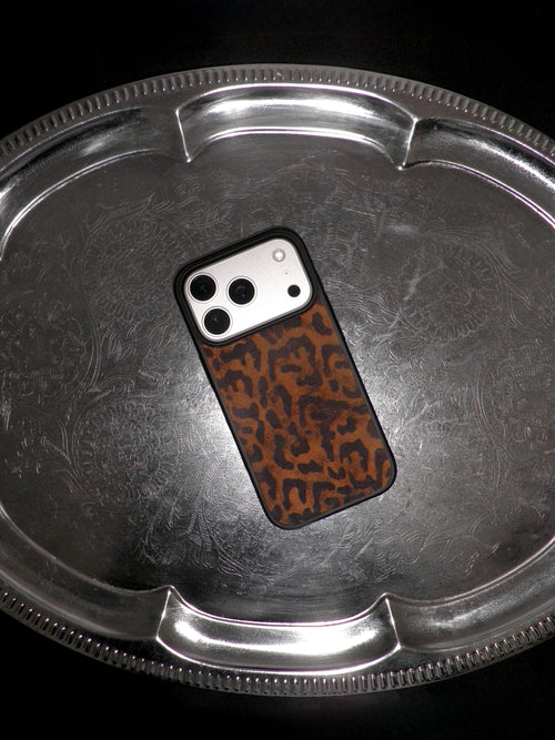 A smartphone case with a brown and black leopard print pattern, shown on a silver metal tray against a black background.